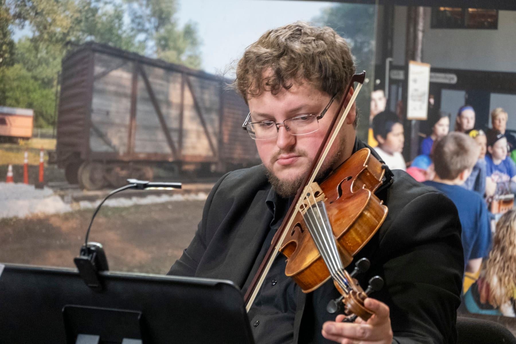 Violinist performing beside a projected image of a freight railcar