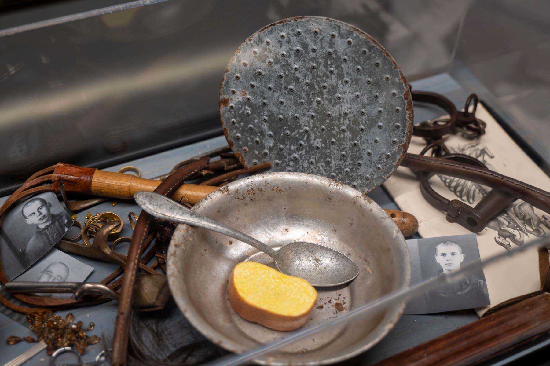 Metal bowl, ladle, perforated disk, and other artifacts in a glass display case.