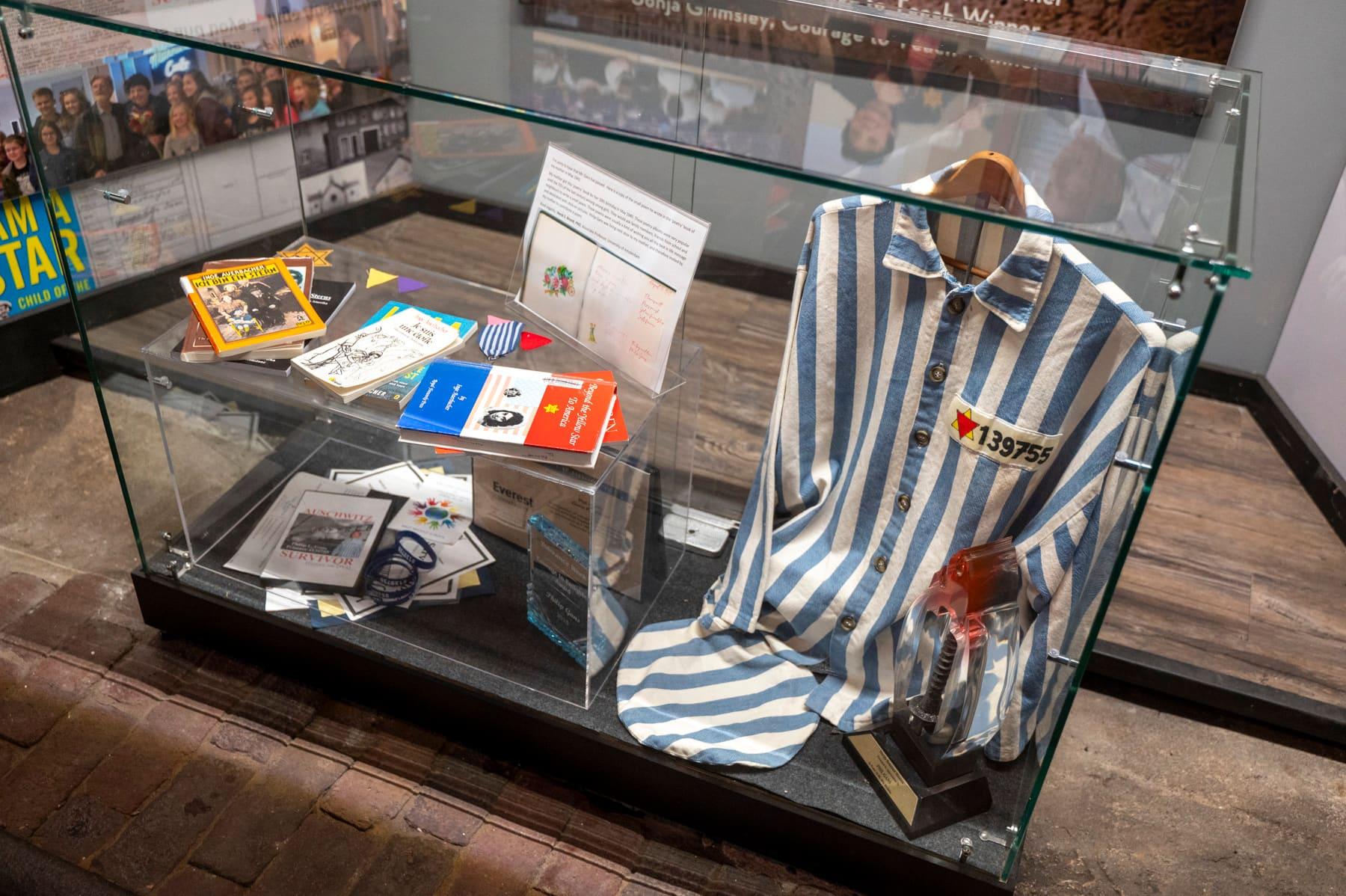 Striped concentration-camp uniform and artifacts in a glass display case