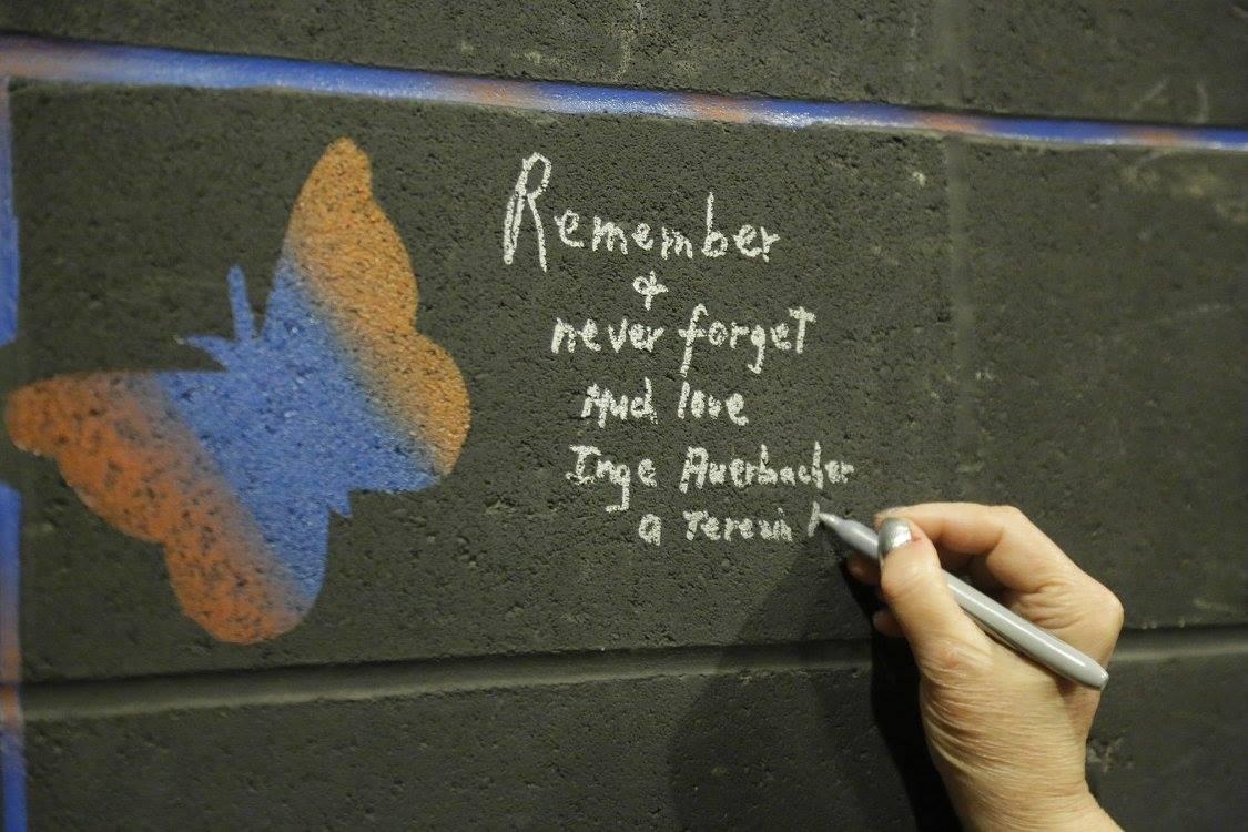 A hand writes a remembrance message in chalk beside a colorful butterfly.