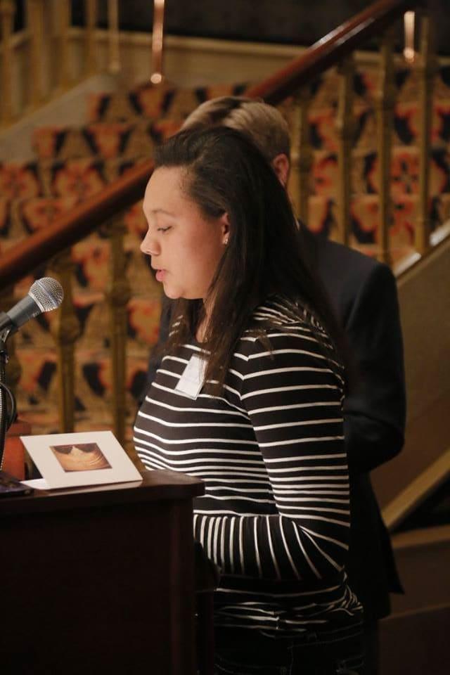 An adult reads from papers at an ornate wooden lectern.