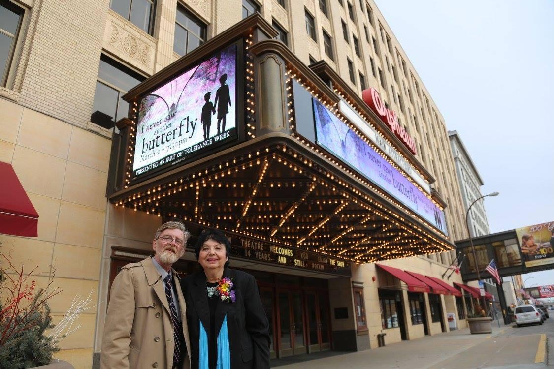 Two adults pose beneath a theater marquee.