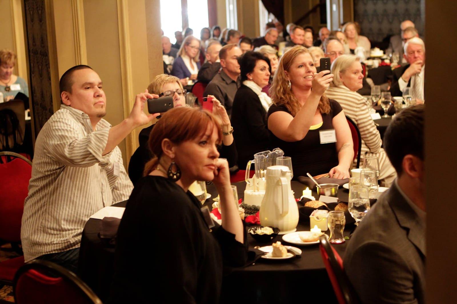 Banquet guests applaud from tables in an ornate room.