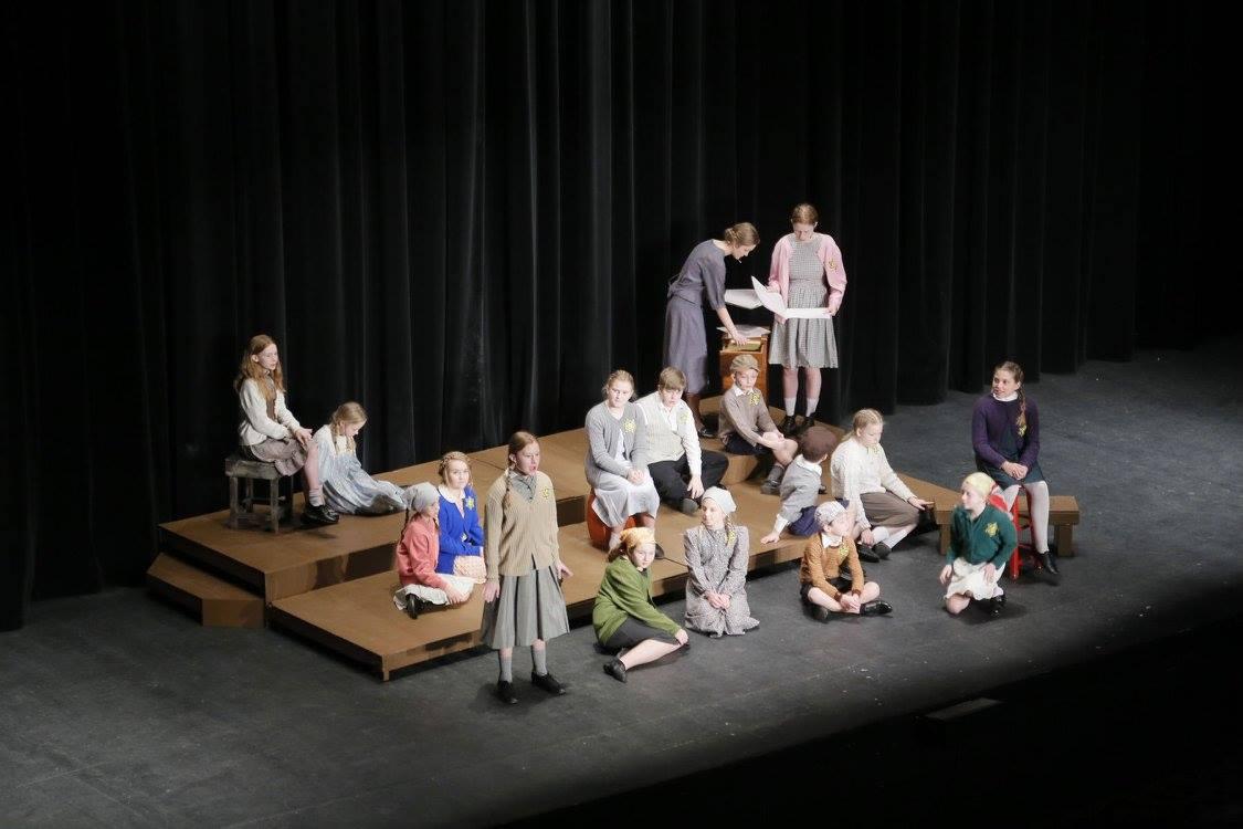 A group of performers gather around benches on a bare stage.
