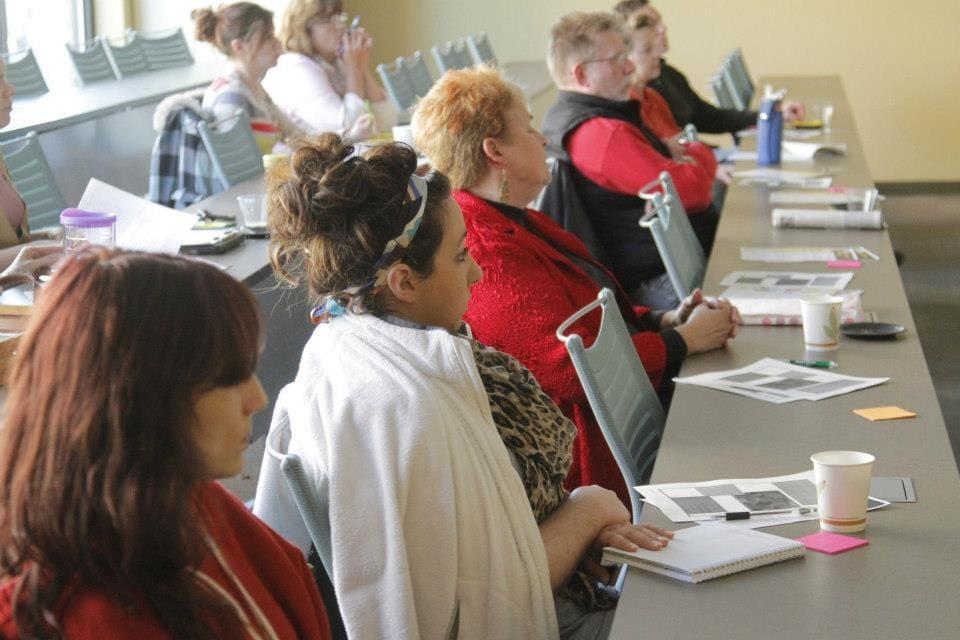 Adults sit along a table covered with workshop materials.