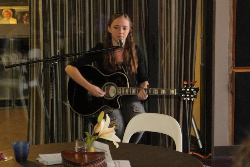 An adult sings and plays acoustic guitar at a microphone.