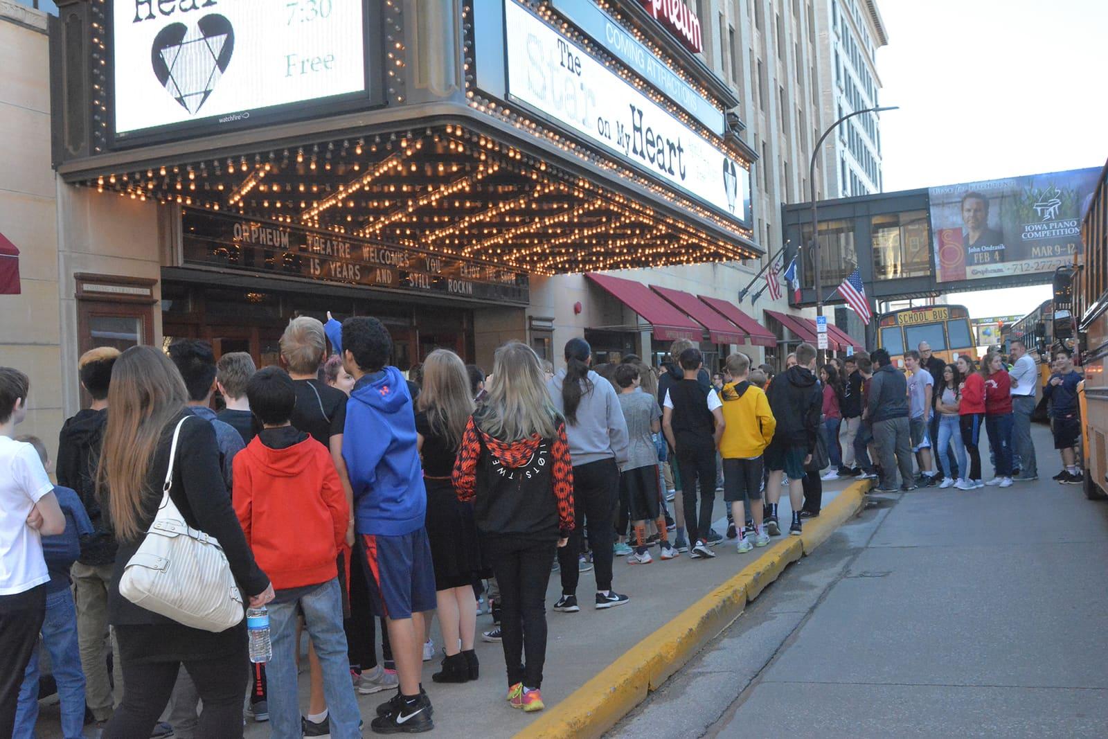 A crowd lines the sidewalk outside a theater.
