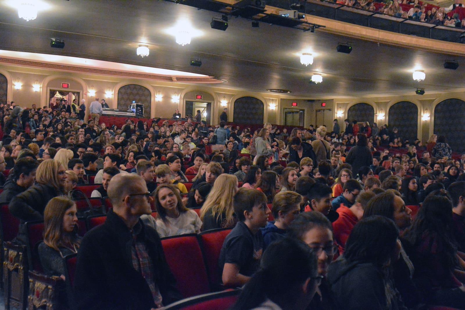 A large audience fills an ornate theater.