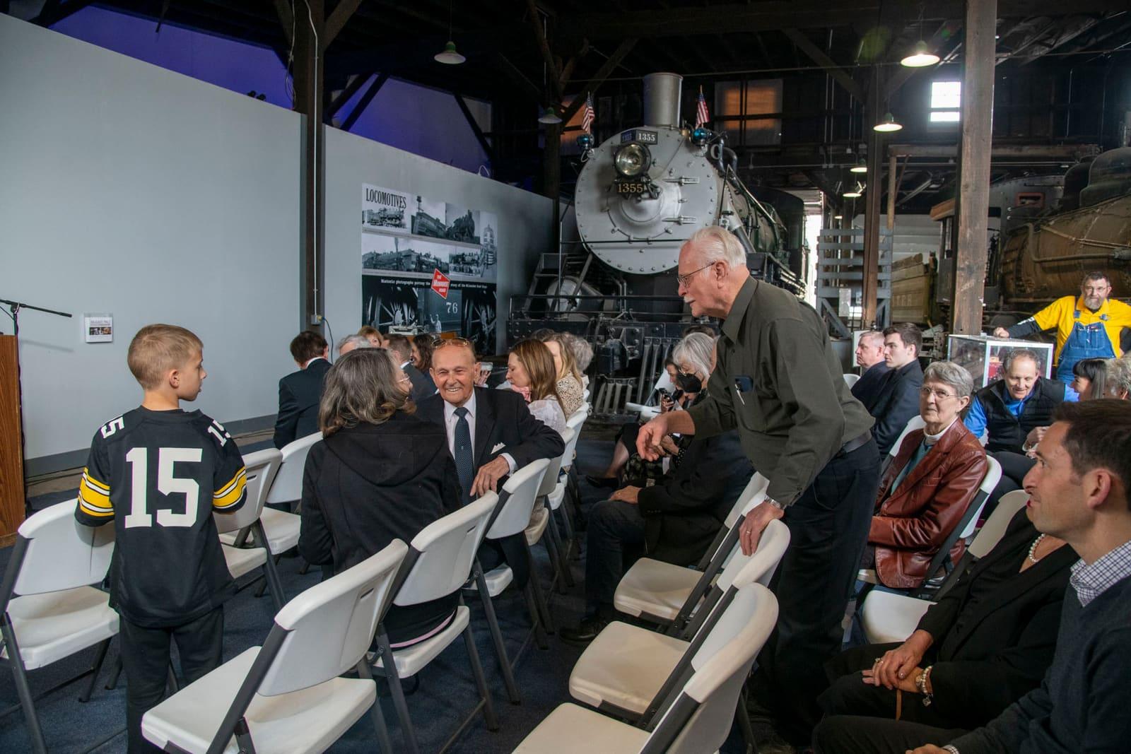An adult leans toward seated attendees in an industrial event space.