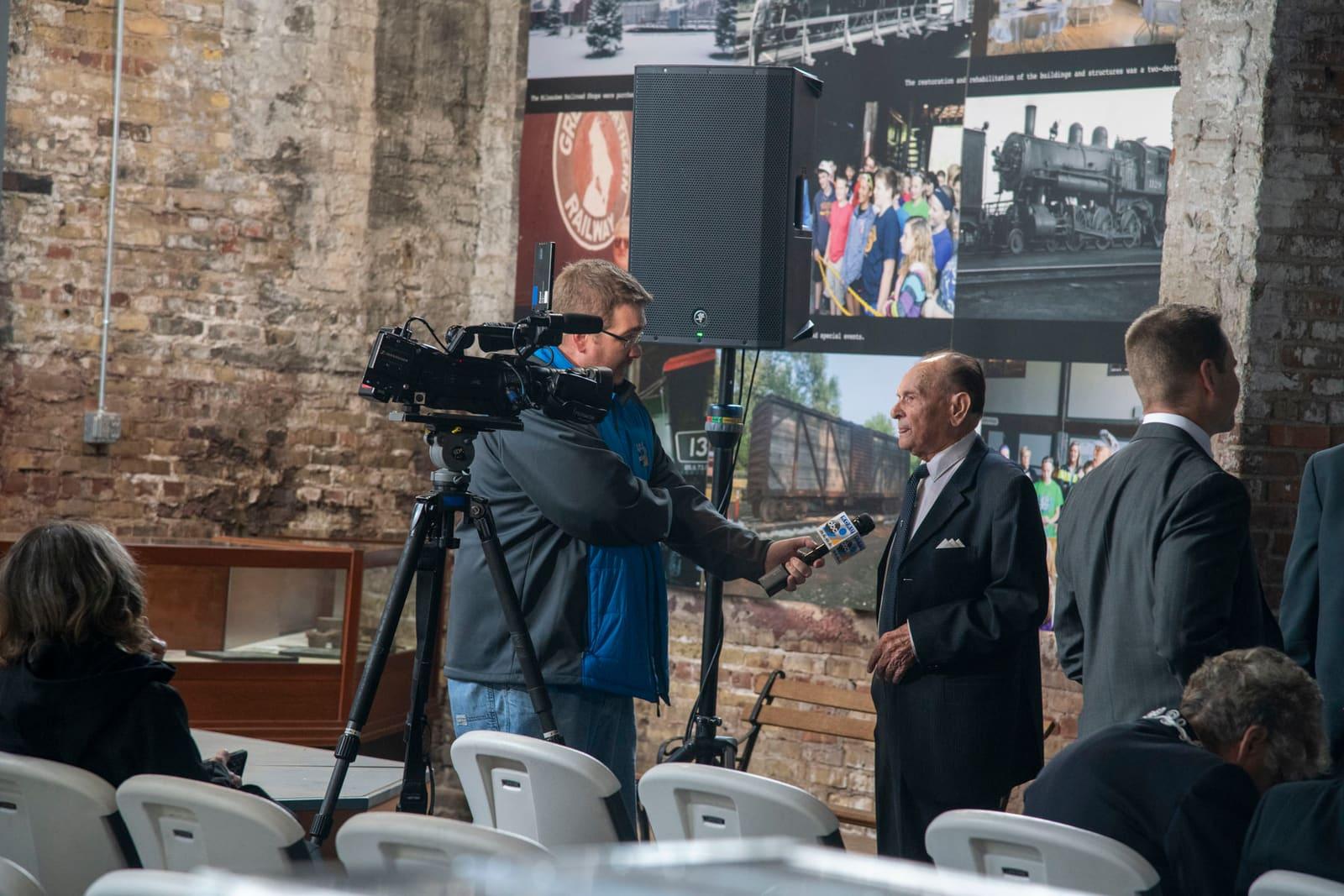 A camera operator films two adults at an indoor event.