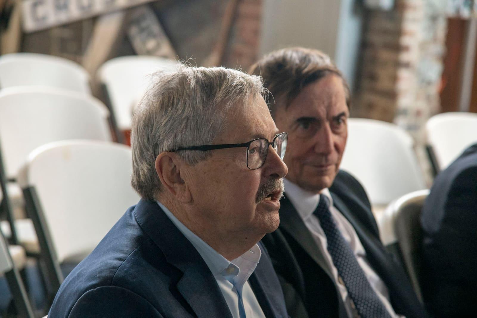 Two seated adults talk during an indoor gathering.