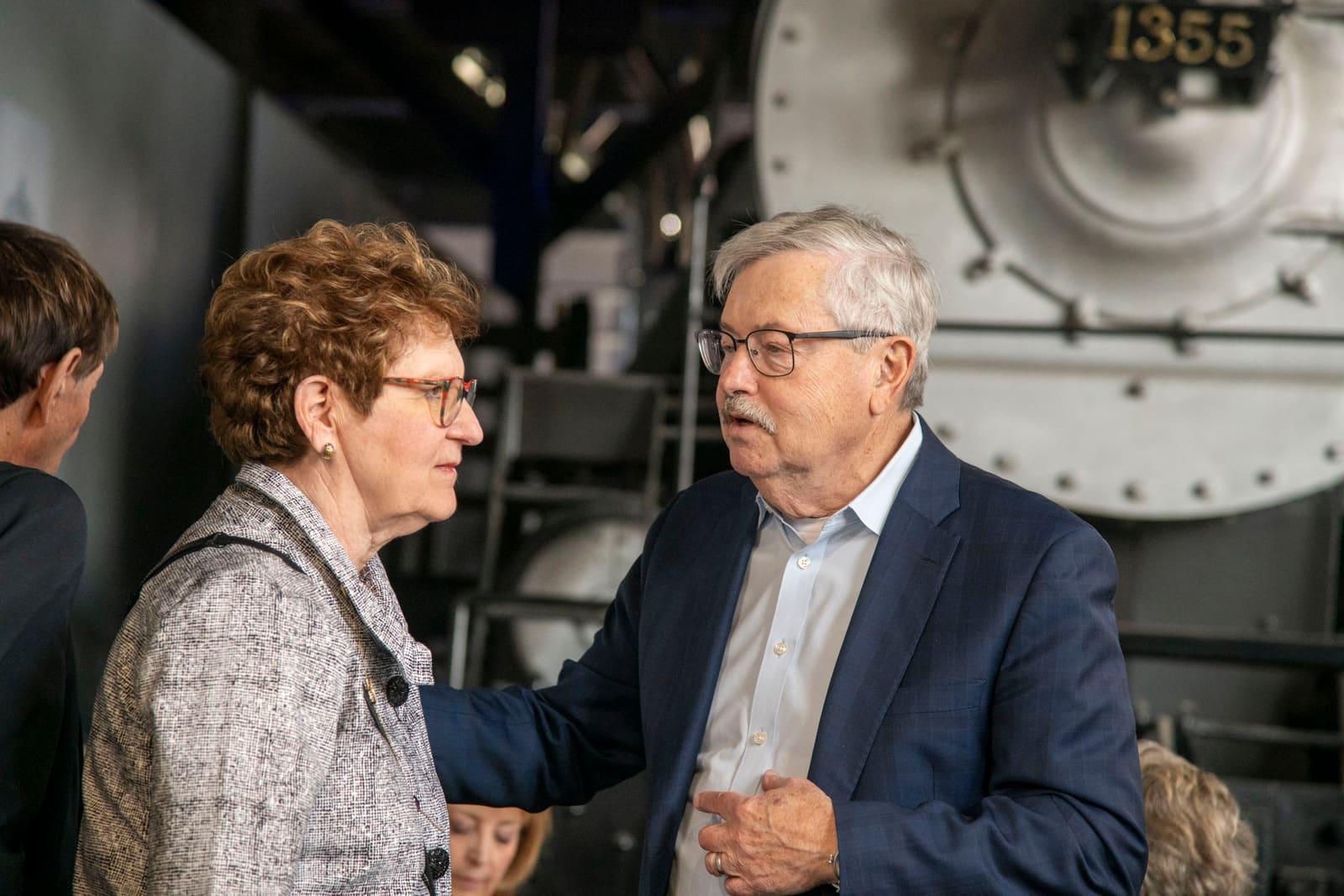 Two adults converse beside large railway machinery.