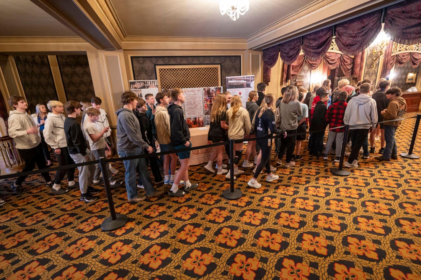 Visitors wait in a roped line across an ornate theater lobby.