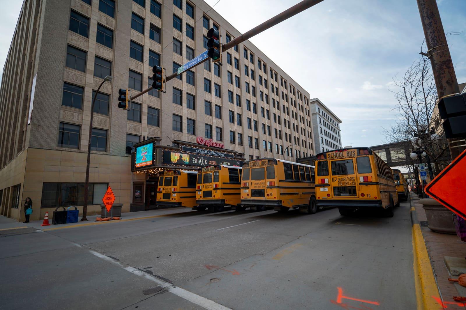 Yellow school buses travel along a downtown street.