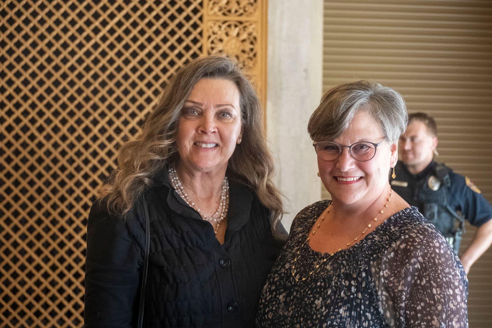 Two adults smile while posing together indoors.