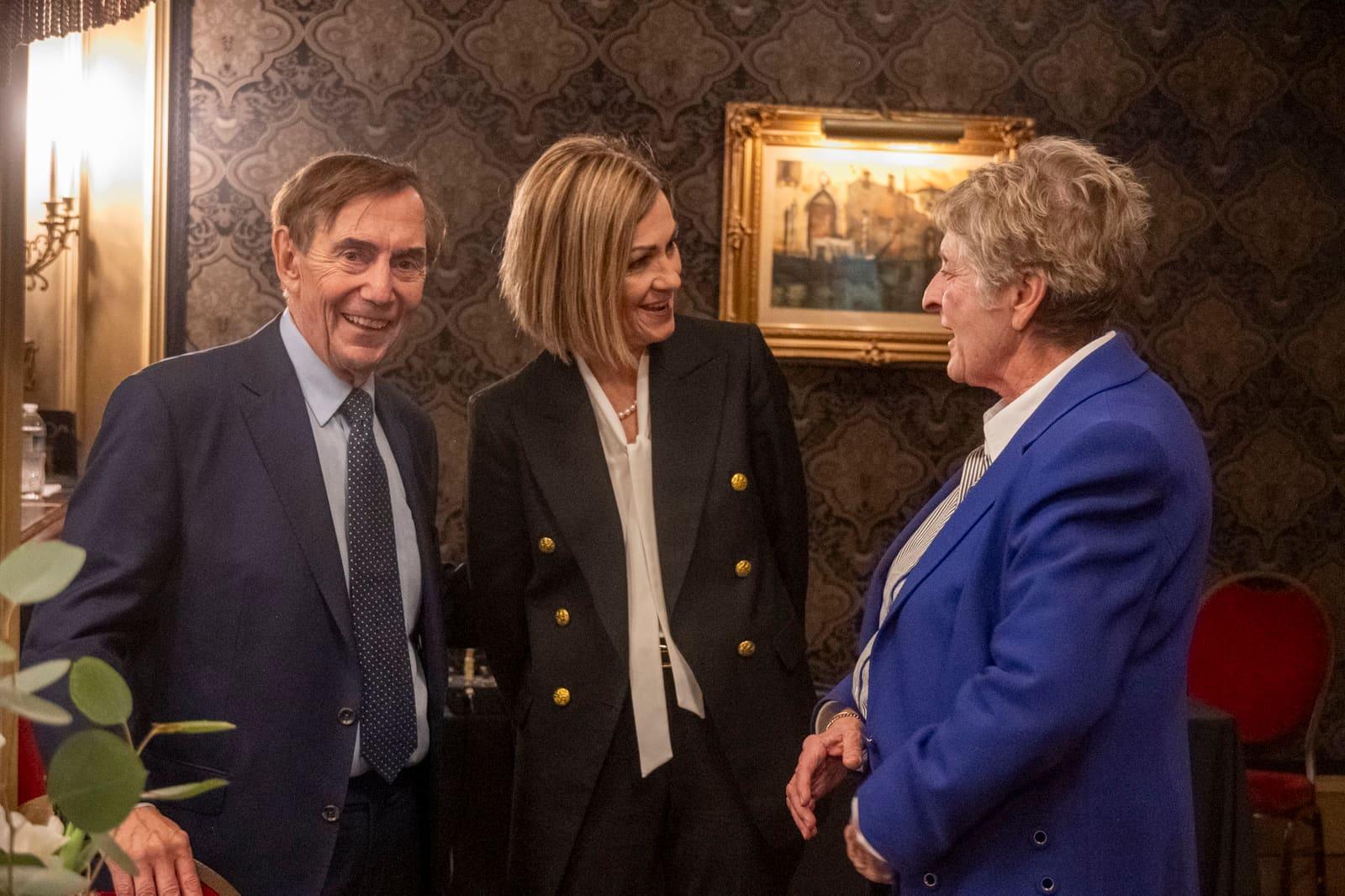 Three adults converse in an ornate room.