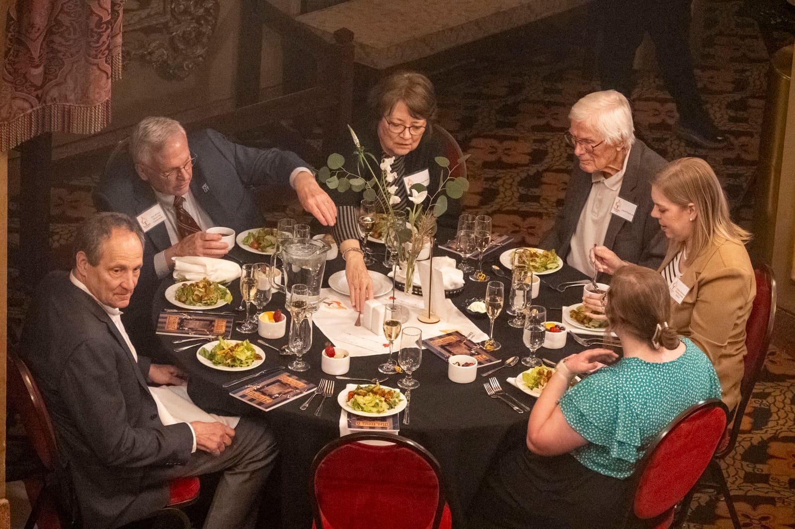 Six guests sit around a candlelit banquet table.