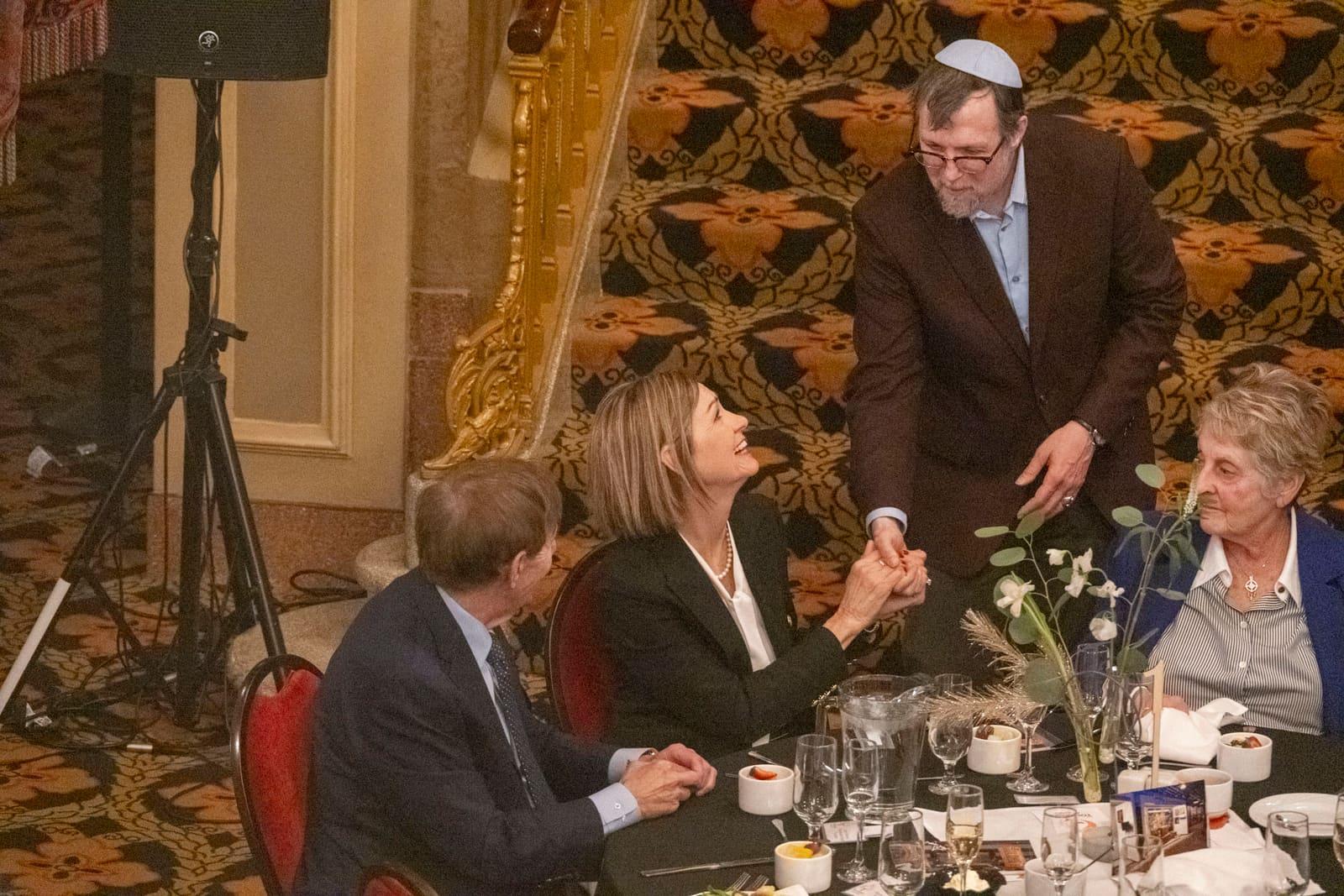 A standing adult laughs with seated banquet guests.