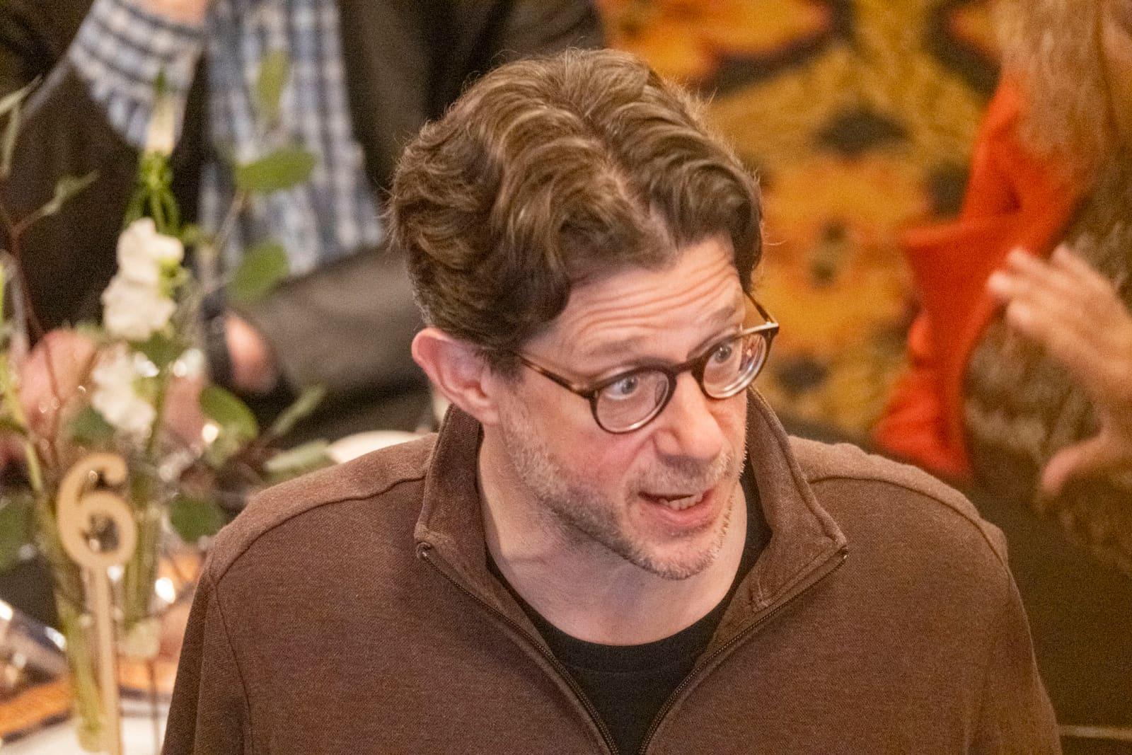 Close-up of an adult with glasses seated at a banquet.