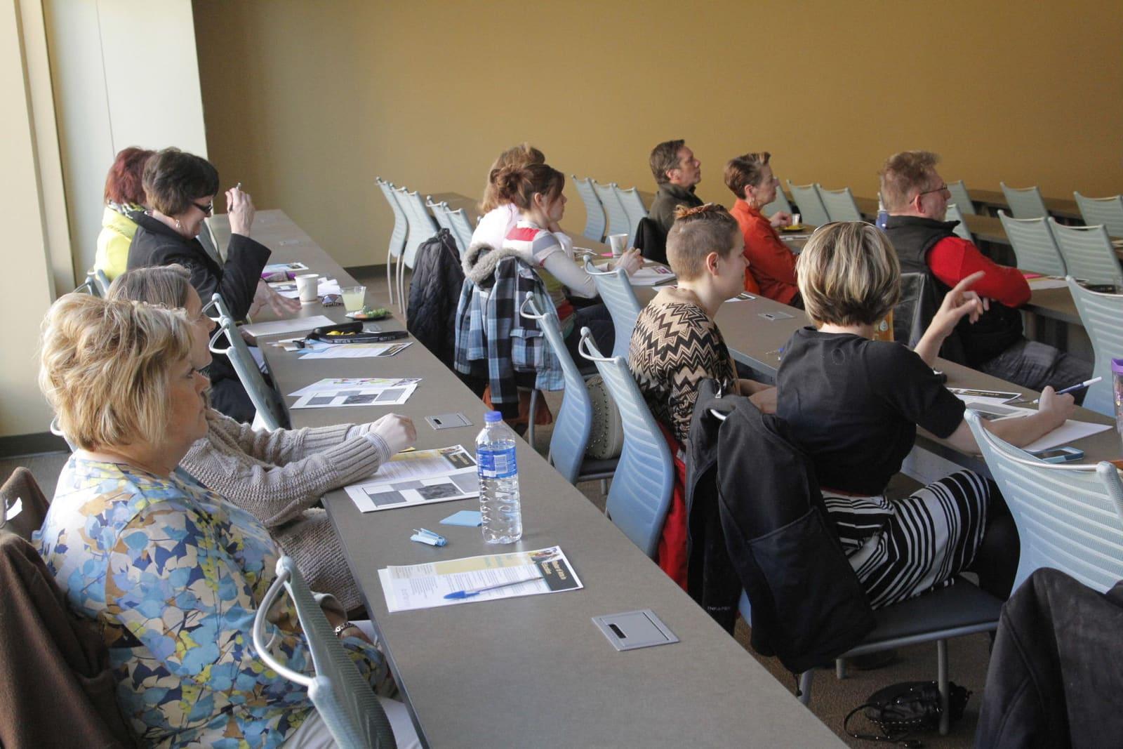 Adults sit around classroom tables with papers and folders during a workshop.