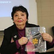 An older woman sits holding up an illustrated book with a yellow star on its cover.