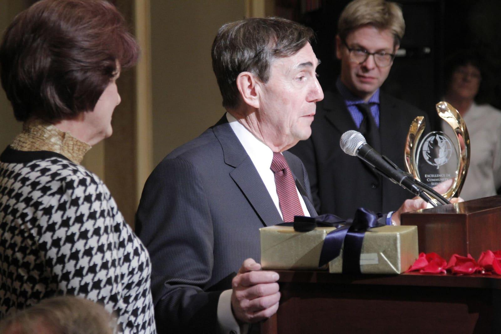 A man at a lectern holds a boxed award while a woman faces him.