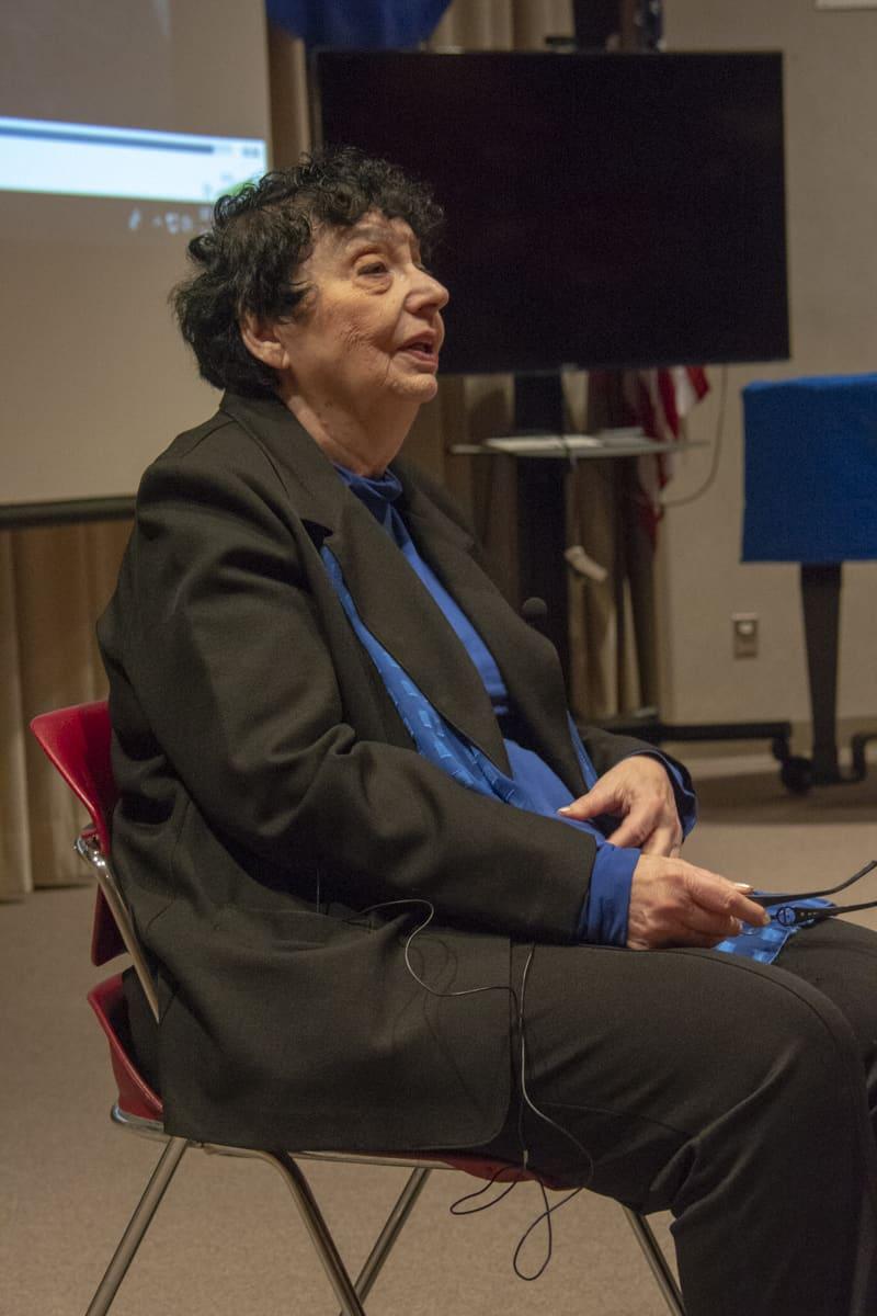 A seated adult smiles while speaking in a classroom.