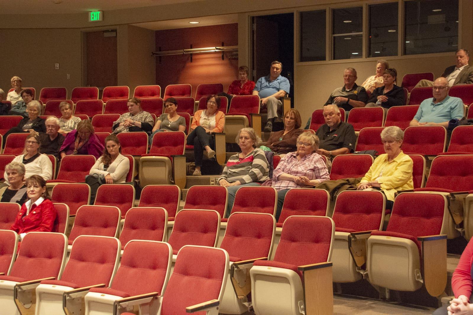 Adults sit among rows of red auditorium seats.