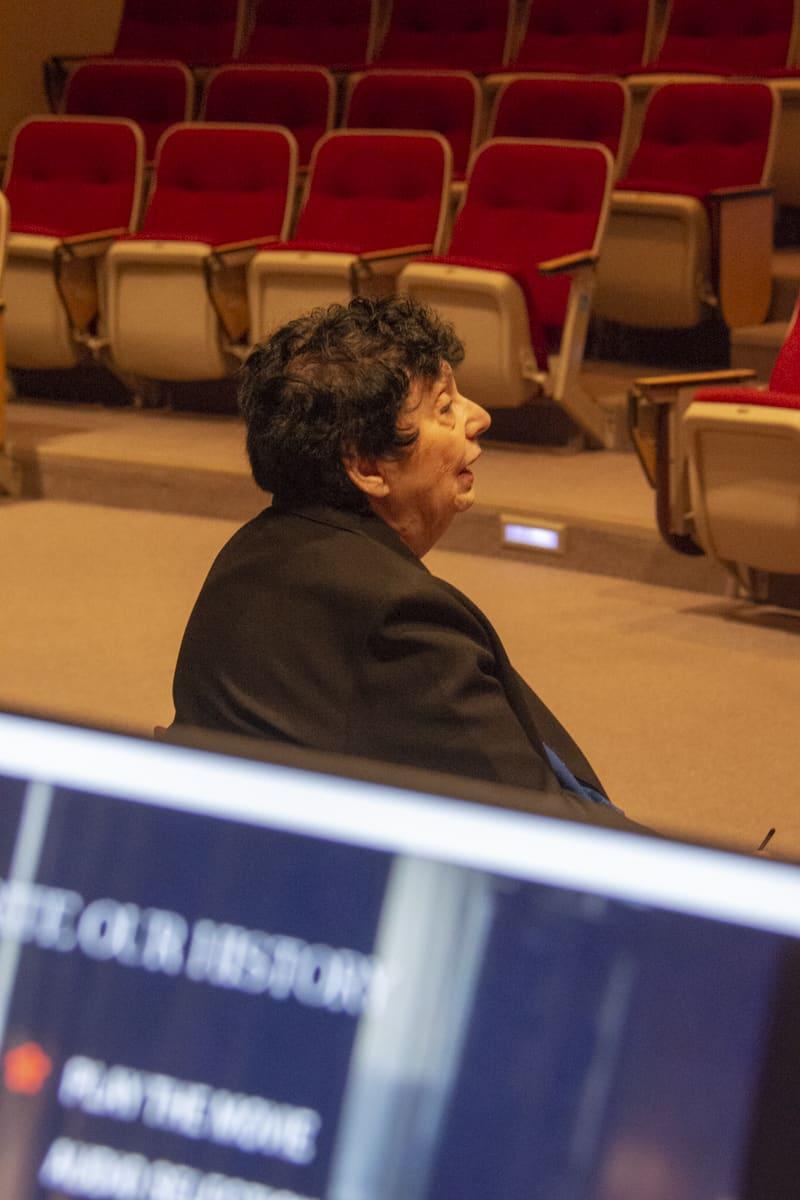 An adult sits near the front of an auditorium with red seats.