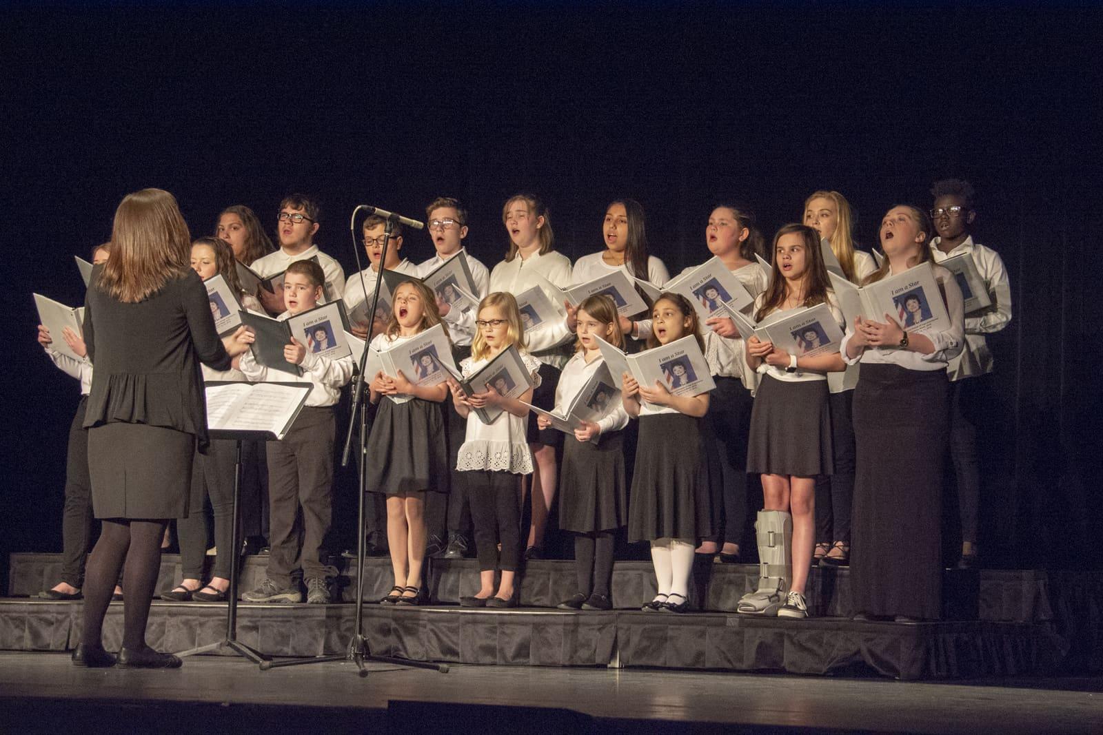 A conductor leads a student choir onstage.