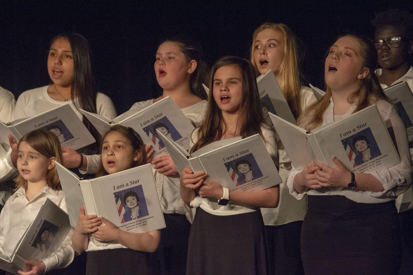 Students sing while holding programs printed with a portrait.