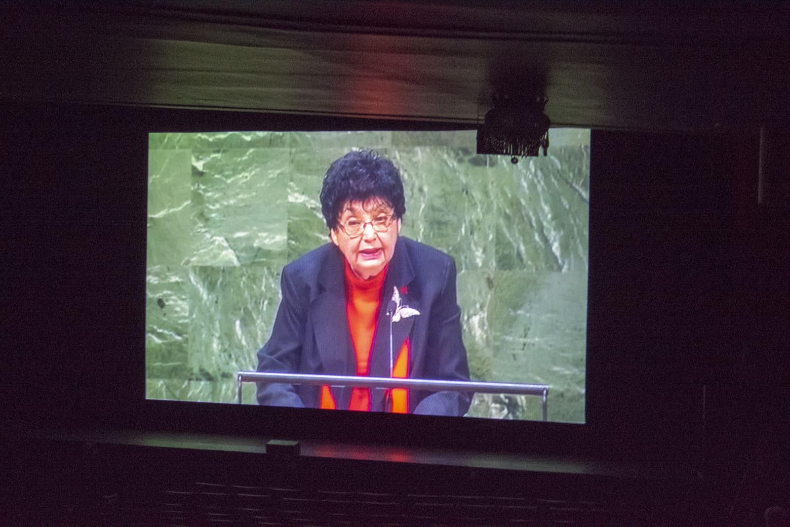 A projection screen shows an adult speaking outdoors.
