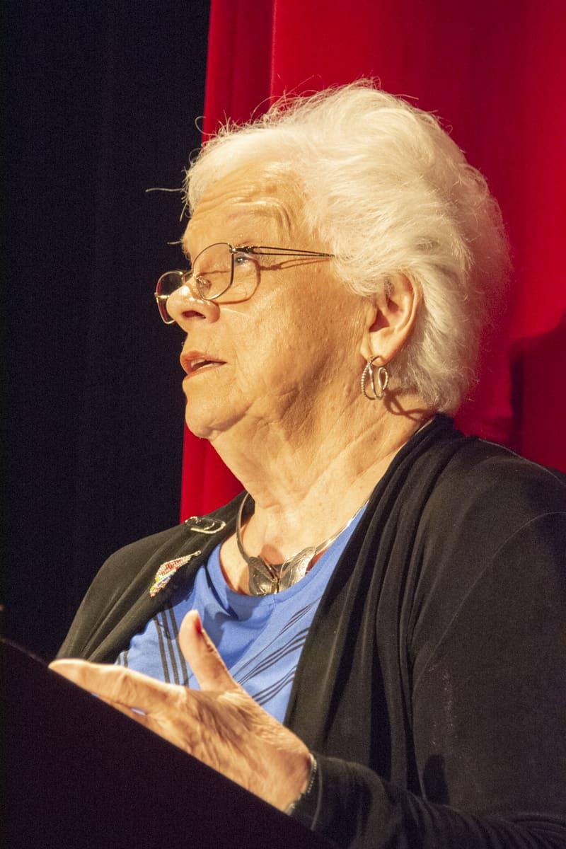 An adult gestures while speaking onstage.