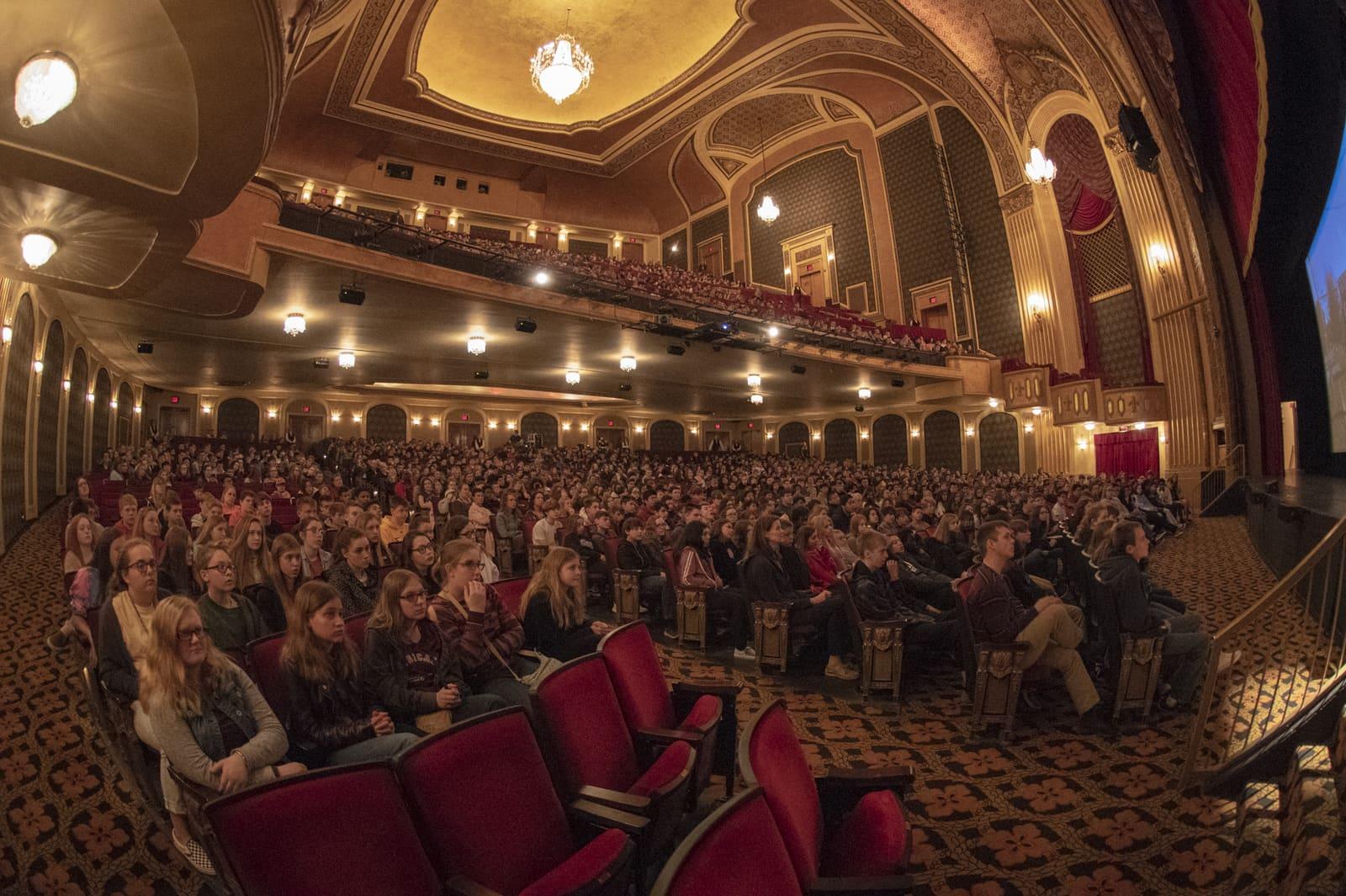 A large crowd fills the main floor and balconies of a theater.