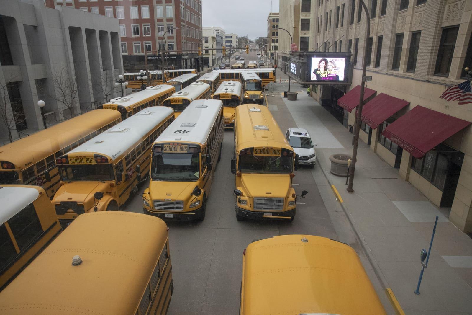 School buses pack a city street between tall buildings.