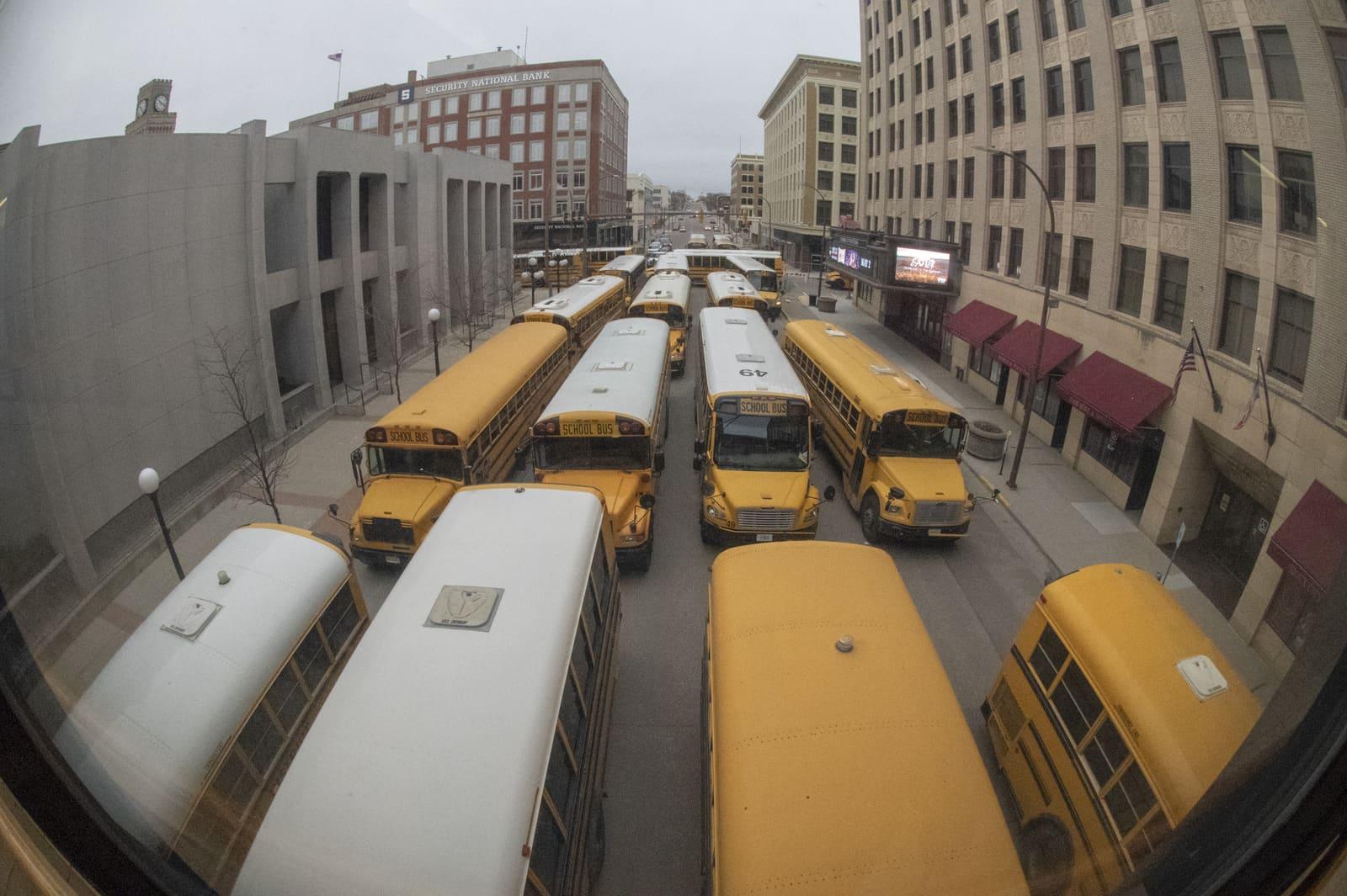 An overhead view shows school buses filling a downtown block.