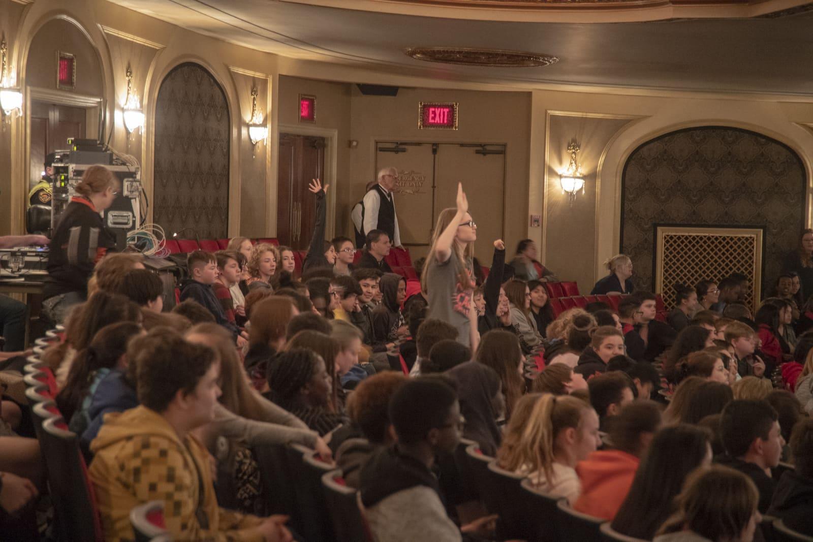Audience members sit in a theater as one person raises a hand.