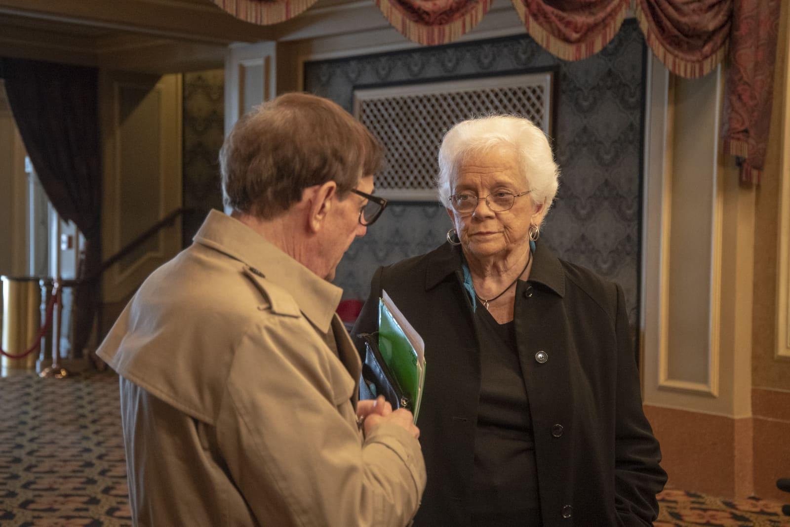Two adults converse in an ornate room.
