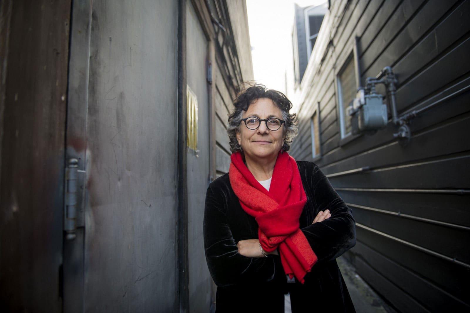 An adult in a red scarf stands in a narrow outdoor passage.