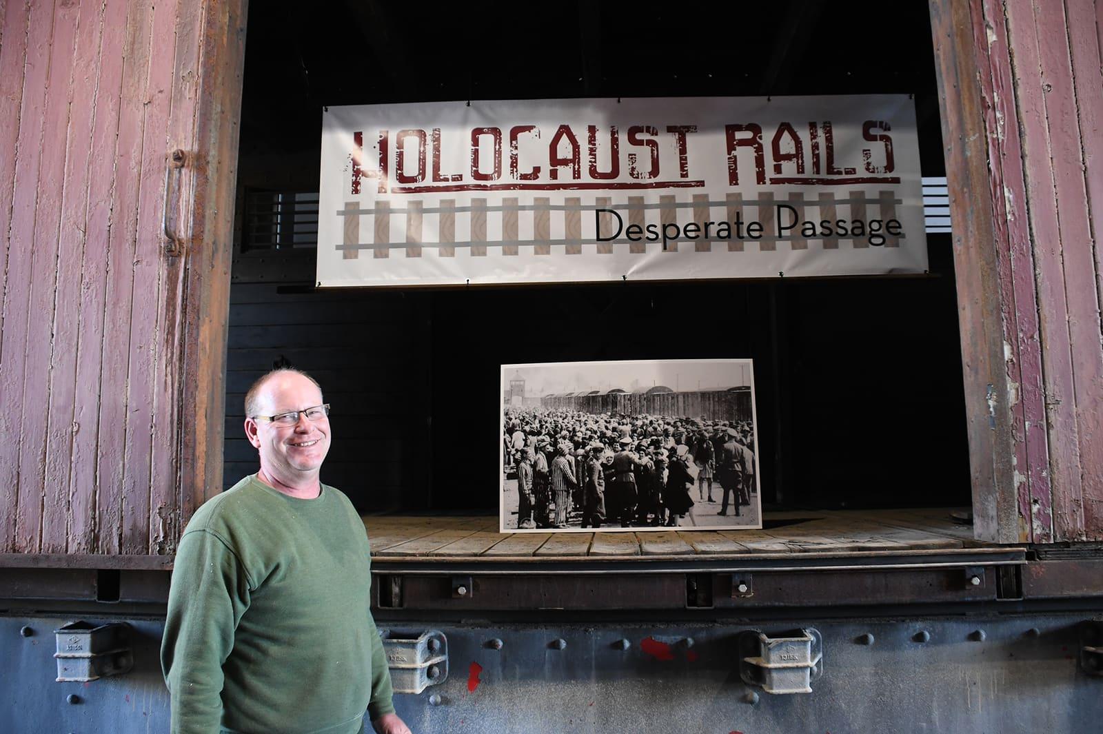 An adult stands before an open railcar doorway beneath a Holocaust Rails sign.