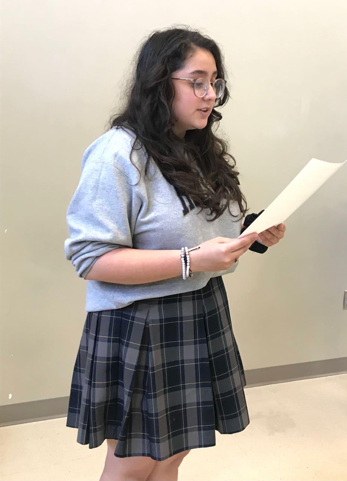 A student reads from a sheet of paper in a classroom.