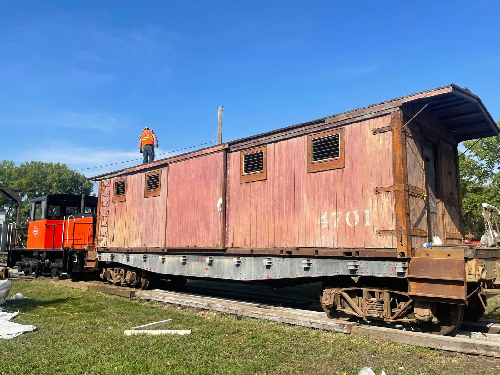 A weathered wooden railcar stands outdoors on tracks.
