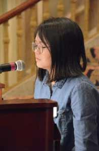 An adult speaks into a microphone at a wooden lectern.