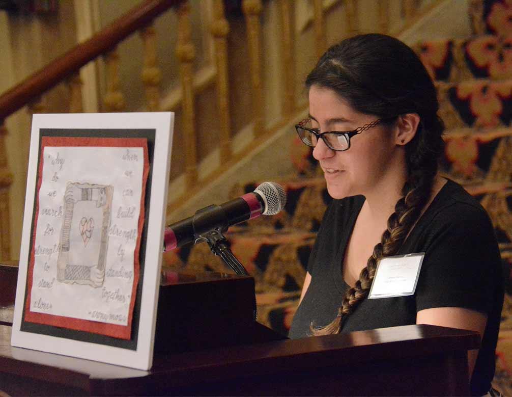 A student reads at a microphone beside framed artwork.