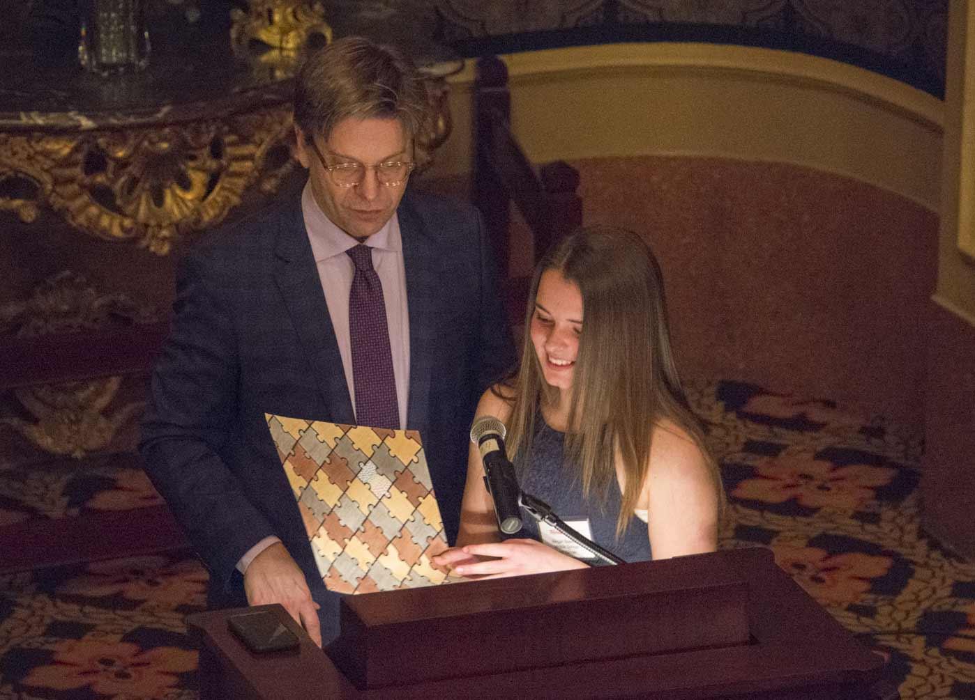 An adult and a student stand at a lectern holding geometric artwork.
