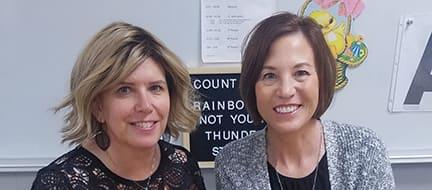 Two adults pose in a classroom.