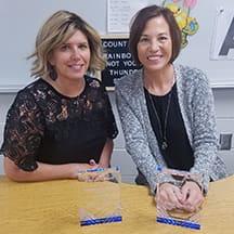 Two adults stand behind a classroom table.
