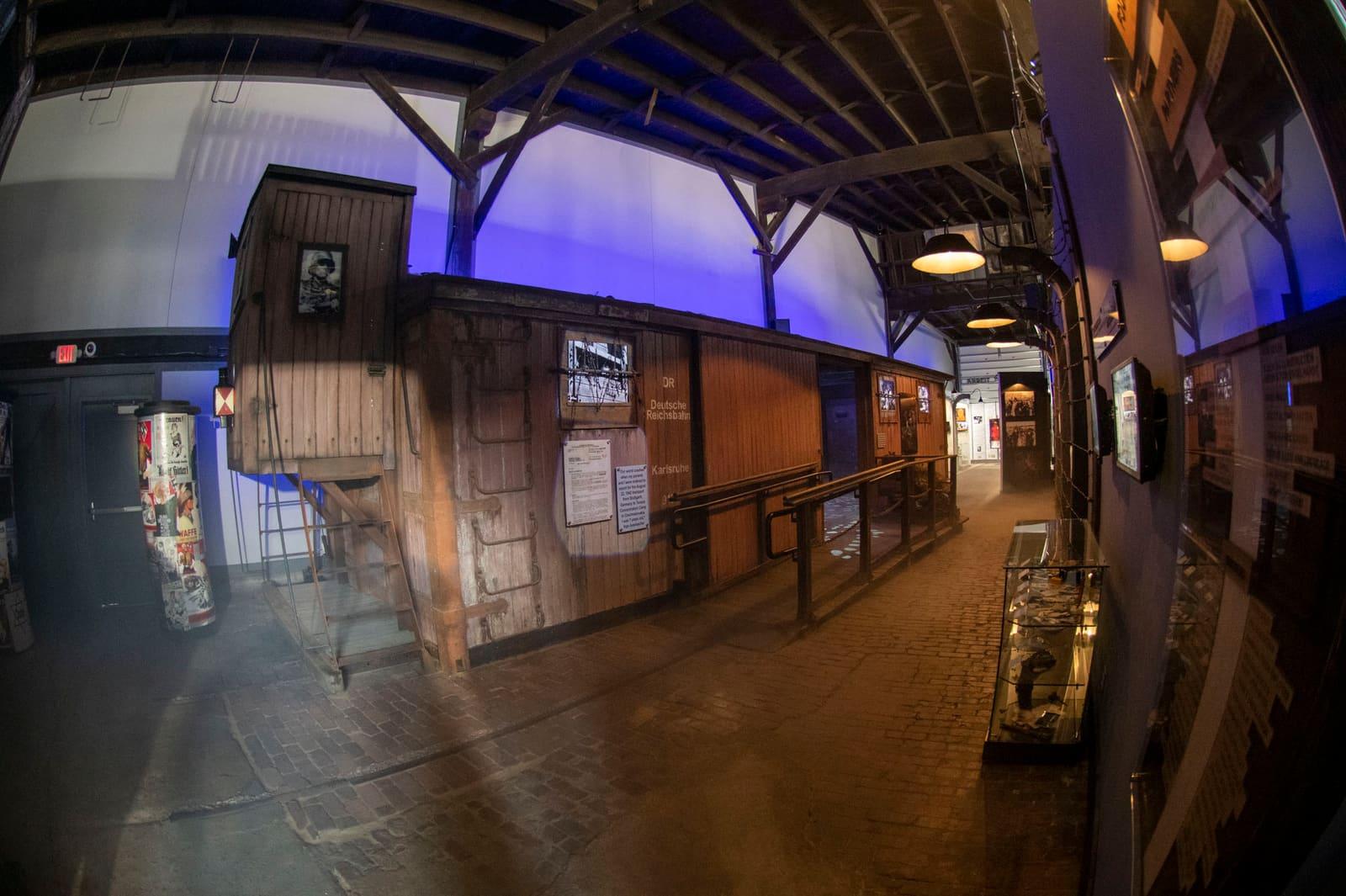 A blue-lit exhibit corridor runs beside a wooden railcar wall.