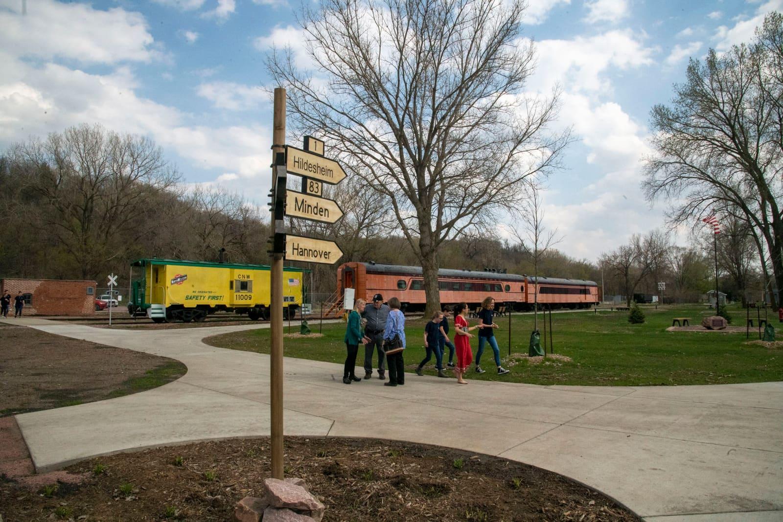 People gather outdoors near a signpost and a green vehicle.