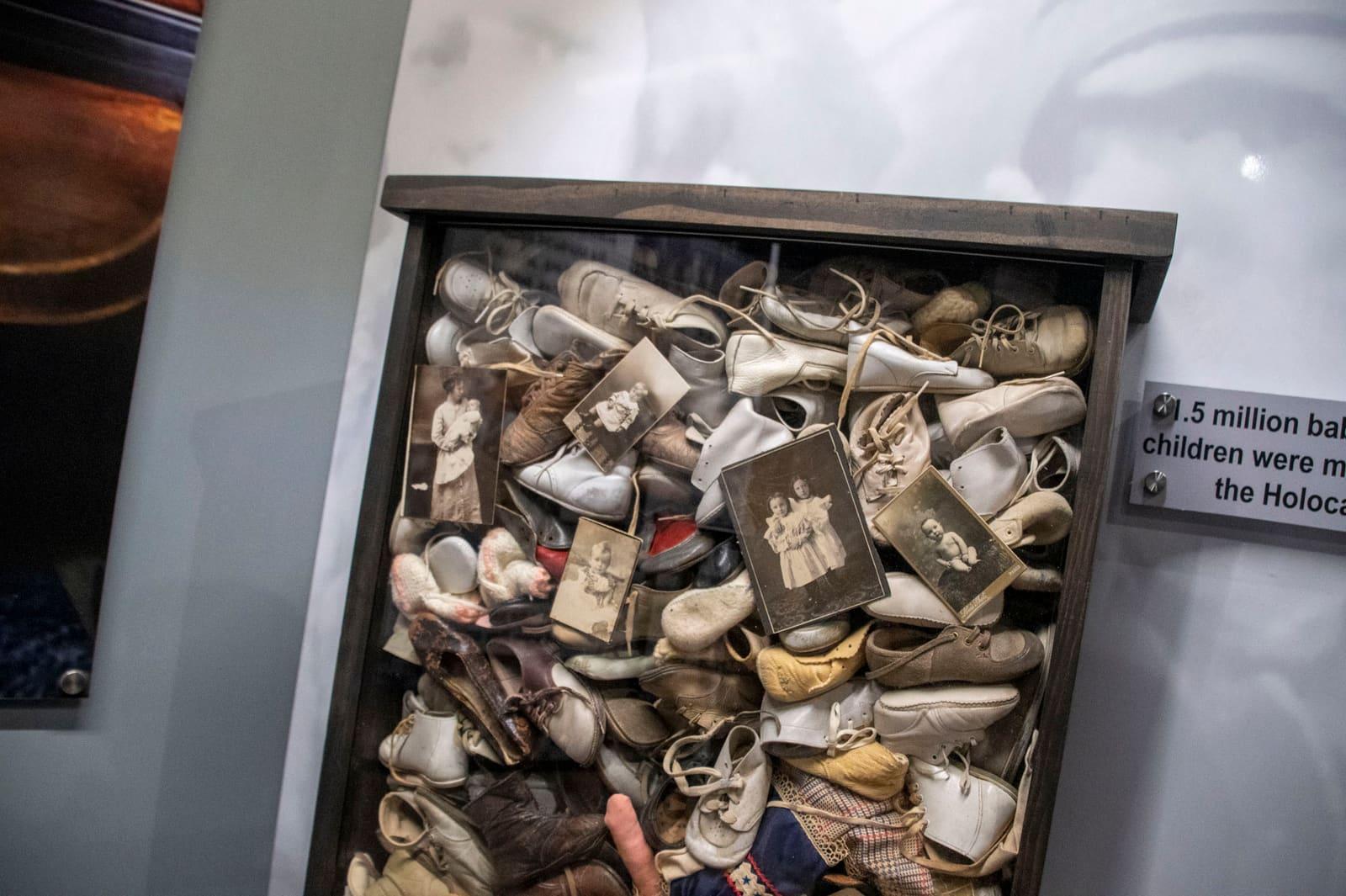 A display case contains many small worn shoes and personal artifacts.